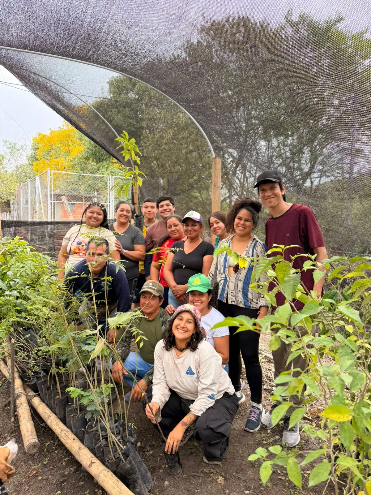 Familias de la vereda posan sonrientes en el vivero, entre plántulas en bolsa, bajo la malla de sombra.